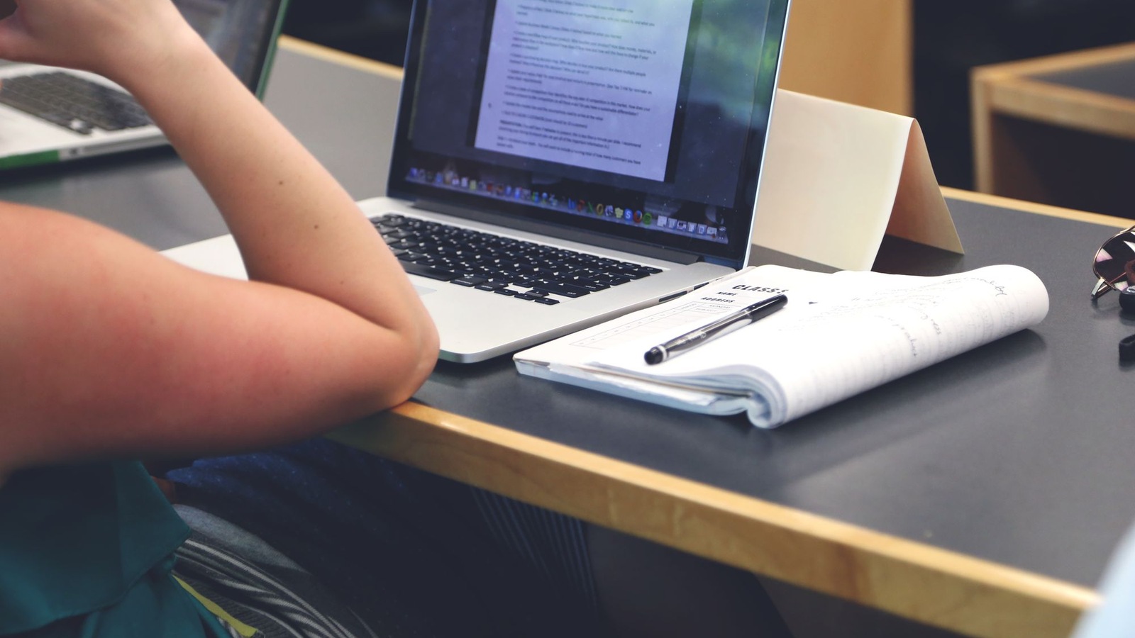 A person pauses over an open notebook beside a laptop.