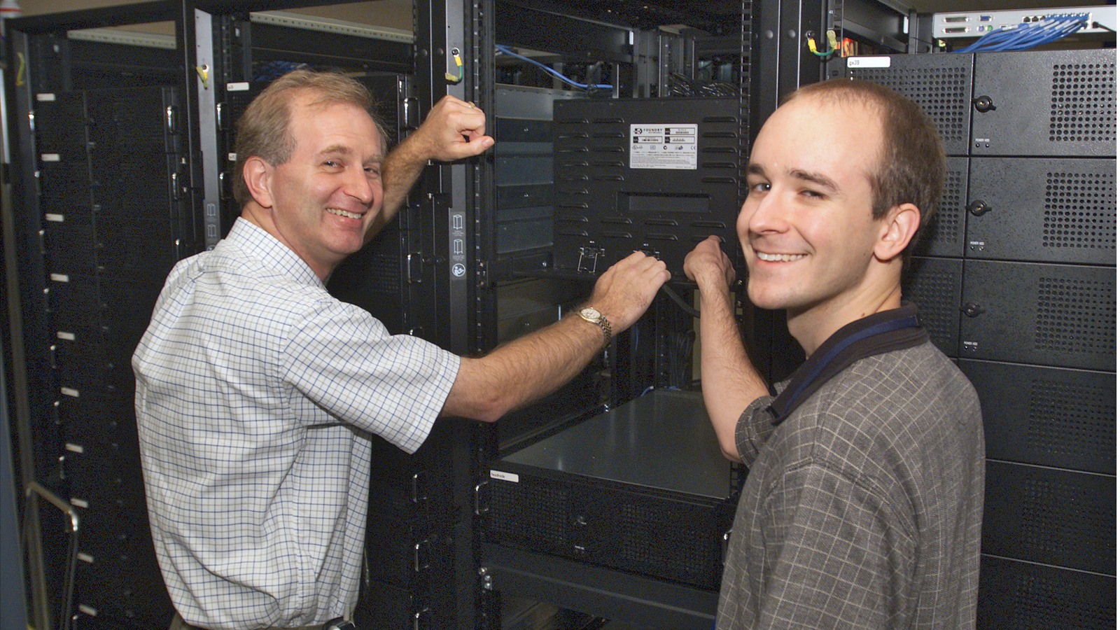 Two technicians inspect computer racks in a research computing lab, representing human evaluation of powerful systems before release.
