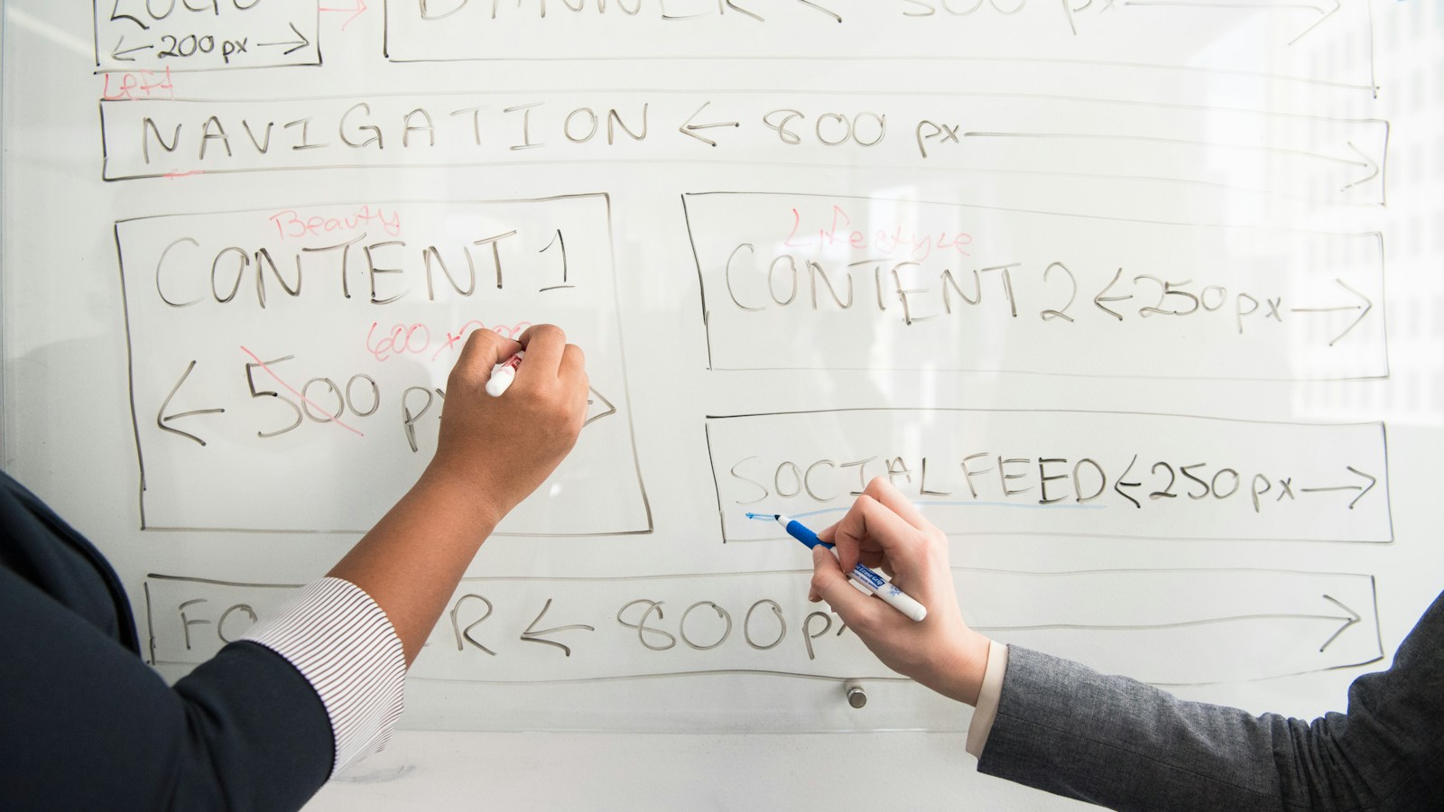 Two people revise measurements on a whiteboard plan, with one number crossed out and replaced.
